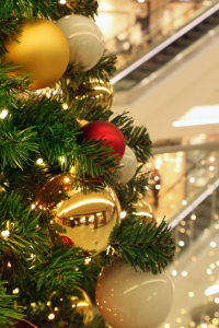 A small glimpse of a Christmas tree with balls of gold, white, and red. In the background is an escalator.