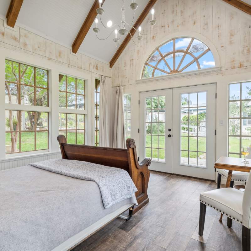 The beautiful outdoors is visible through the vintage windows. The light, airy bedroom with queen bed and a church pew at the foot serves as a place for luggage.  