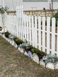 White picket fence with flowers planted in front of it bordered with repurposed dinner plates.