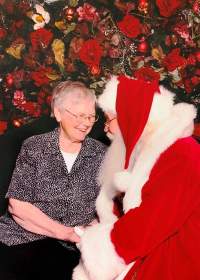 An elderly lady and Santa grasp hands and share a conversation.