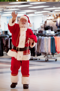 A mall Santa Claus waving. A department store with clothes racks in the background.