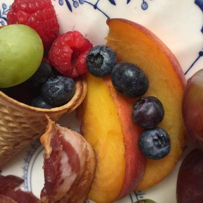 Fresh hand-cut fruit in a cone Fresh fruit in a cone with a dab of fresh-made whipped cream served on a blue and white floral China plate.
