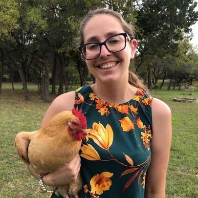 Female guest wearing a green dress with yellow flowers smiles as she holds a yellow hen.