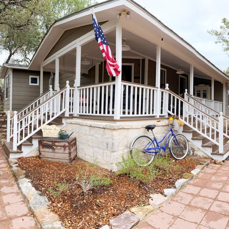 Front of small house with elevated porch, white railing, and three sets of steps with side rails.