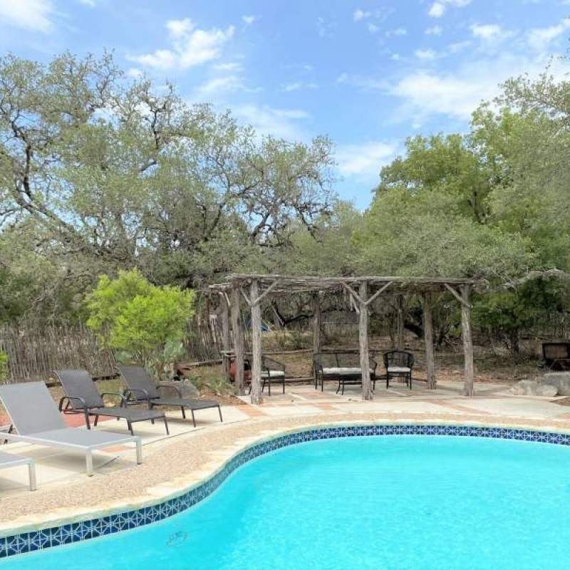 Swimming pool with four poolside chaise lounge chairs and a cabana in the background with seating.