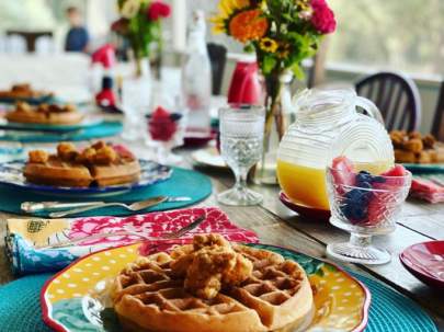 Bellavida hearty homemade breakfast. A beautifully set table with fresh flowers, orange juice, hand-cut fruit and a plate of homemade waffles topped with fried chicken.
