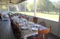 Huge screened porch with large farmhouse style table and chairs set for a meal with beautiful dishes.