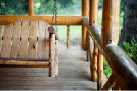 Natural wood porch swing surrounded by wood railing.