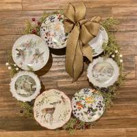 Wall wreath of china plates with winter scenes, greenery, and a burlap bow.