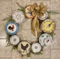Wreath of china plates with rooster images encircled with greenery and a burlap bow.