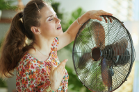 Woman with her hand resting on a large circular fan trying to cool off.