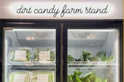 Commercial style refrigerator with see-through glass doors. Inside and clear packages filled with mixed micro greens and other fresh produce.