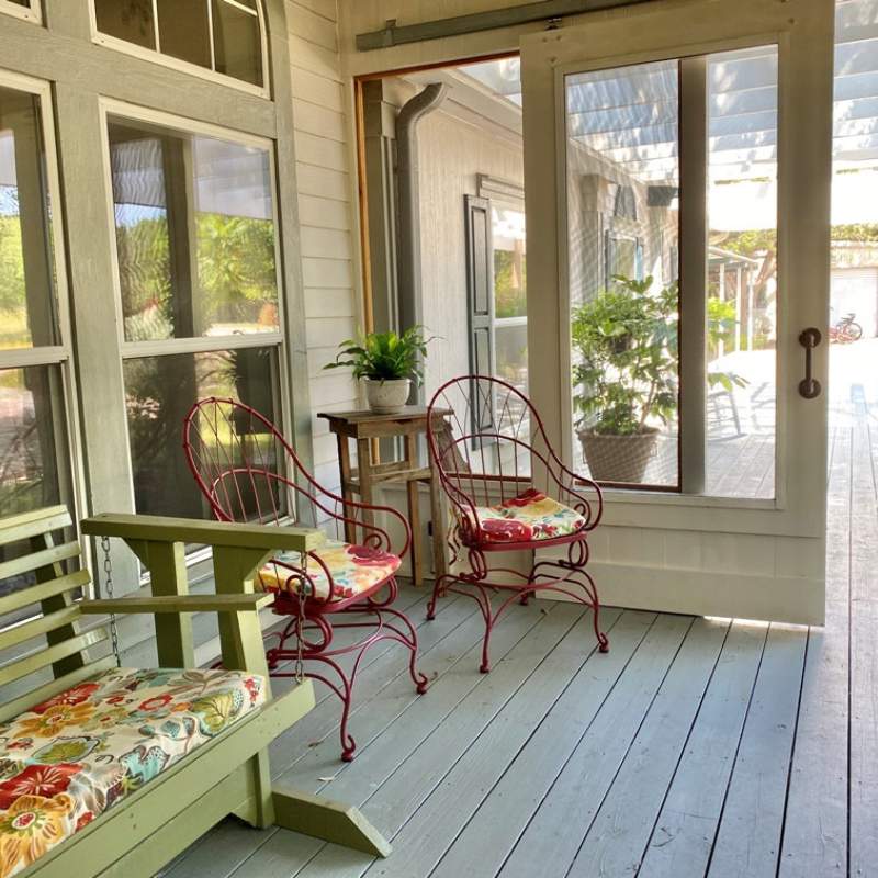 Inviting screened front porch with barn-style door. Two red side chairs and a green glider bench invite guests to sit for a spell.