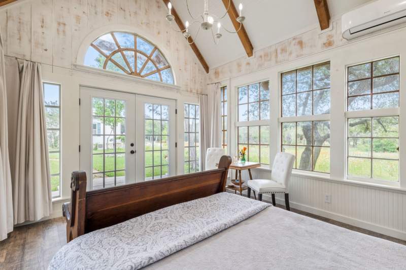 Dreamy escape is surrounded by vintage windows offering panoramic views of the serene Texas Hill Country landscape.