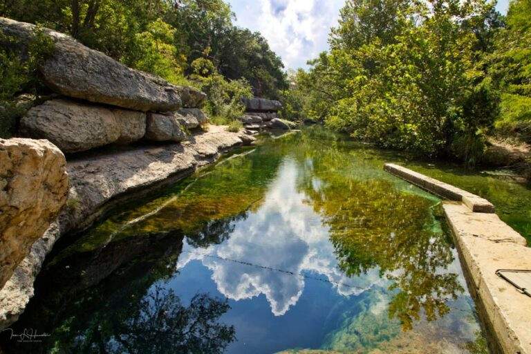 Natural swimming hole with blue water and green algae surrounded by large natural rocks.