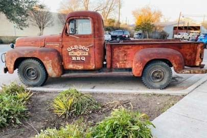 Rusty, red, vintage pickup truck with Old 300 BBQ signage on the door.