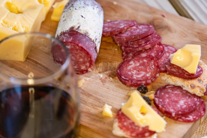 Charcuterie board with cheese, sliced sausage and a glass of red wine.