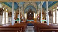 Stunning view of the interior of a 19th Century Catholic Church. A hand painted blue ceiling with floral arches tower above the gothic style wood-stained organ and church pews.