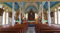 Stunning view of the interior of a 19th Century Catholic Church. A hand painted blue ceiling with floral arches tower above the gothic style wood-stained organ and church pews.