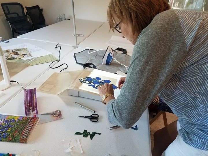 Woman leaned over a table hand-piecing a bluebonnet flower for a quilt  square.