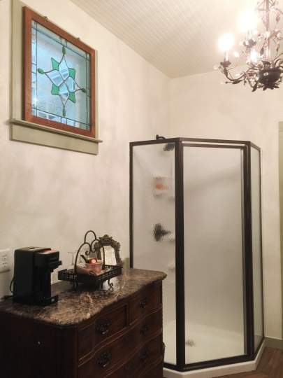 Marble top five-drawer dresser. On the top is a small coffee pot. In the background is an opaque glass step-in shower.