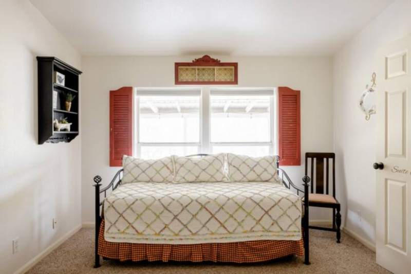Twin daybed with quilt covering and red check bed skirt. Behind it a large window with red shutters on the inside