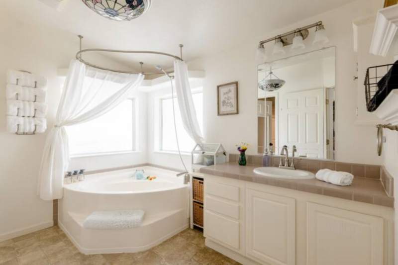 Garden bath tub with shower. Long counter with oval sink. Rolled towels hang in a wine rack on the wall.
