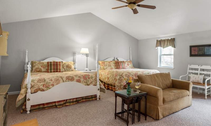 Spacious bedroom with king and queen beds, a sitting area with twin sofa sleeper. Furnishings are farmhouse cottage with whitewashed furniture.