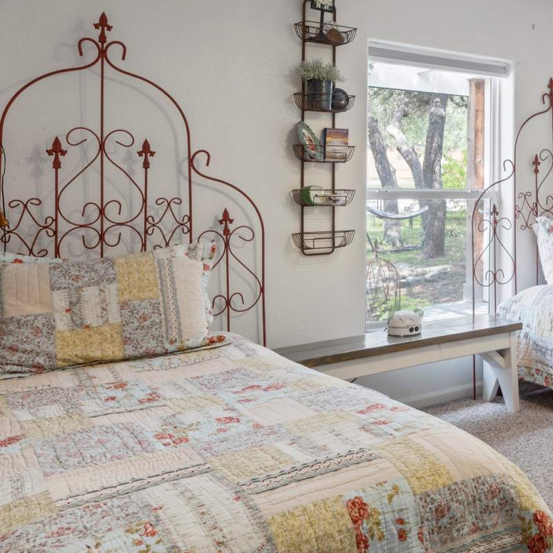Welcoming homey bedroom with two twin beds each with a red metal trellis headboard. Matching patchwork quilts and pillow shams cover each bed.