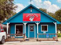 Blue house with porch railing and red sign above door of Tacos El Tizon