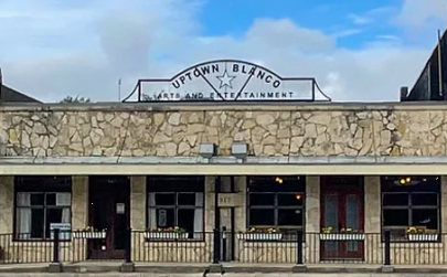Cream color stone historical building with a black metal rail in front. A sign on the roof's edge reads: Uptown Blanco Restaurant