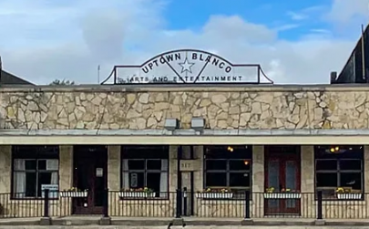 Uptown Blanco Restaurant Cream color stone historical building with a black metal rail in front. A sign on the roof's edge reads: Uptown Blanco Restaurant