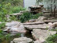 Greenery borders large flat rocks create the base for the small cascading waterfall. 