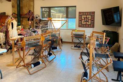 Several floor-style wooden weaving looms set up in a semi-circle for weaving instruction.