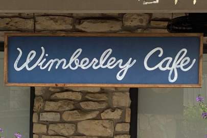 Hanging sign with blue background has words,  Wimberley Cafe in white letters.