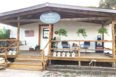 An inviting entrance in Wimberley Gardens. The elevated front porch has a swing and other seating. Hanging plants and birdhouses line an area of the porch.