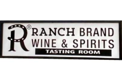 Red round sign with large letter R in the center. Below it a sign with white background and in black the R logo and words: Ranch Brand Wine & Spirits Tasting Room.