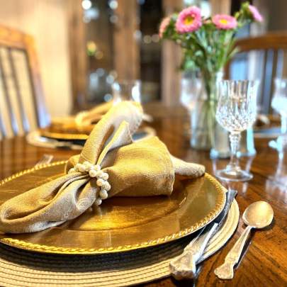BellaVida Breakfast setting Fresh flowers center a table of four place settings. Each gold cloth napkin is secured with a pearl napkin ring, set upon a gold plate charger. Lovely crystal glassware and silver-plate flatware add to the elegance of the table.