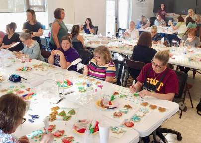 A room full of women decorating sugar cookies with colorful icing.