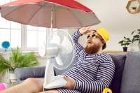 Man sitting in his living room wearing a beach hat and holding an umbrella-fan combination in his lap.