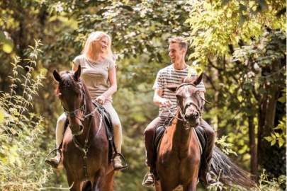 A woman and a man each riding a horse in a heavily wooded area.