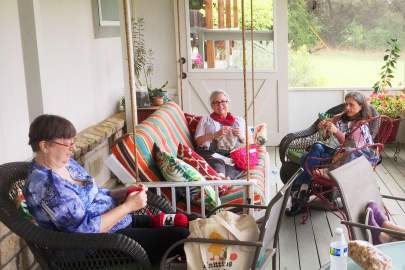 Three women sitting on the screened porch relaxing and knitting.