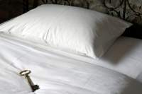 White plush bedding with a white fluffy pillow. On the bad is a skeleton key representing a room key.