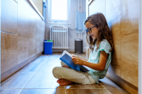 Young girl sitting on a hallway floor reading a book.